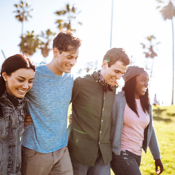 group of friends walking in the sun while smiling, in front of palm trees