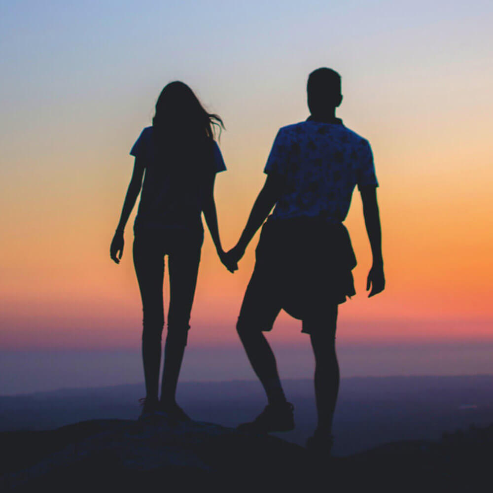 A couple holding hands on a mountain peak, enjoying the breathtaking view.