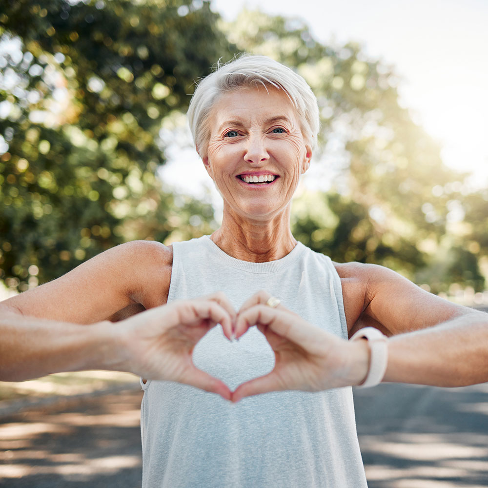 smiling woman in workout attire making heart shape with her hands.