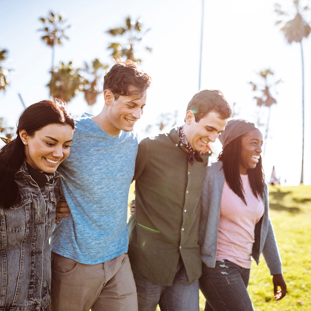 group of friends walking in the sun while smiling, in front of palm trees