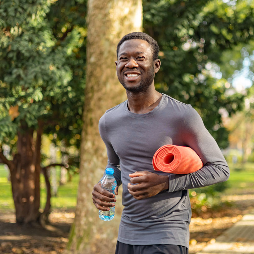 man walking outside with water bottle and yoga mat